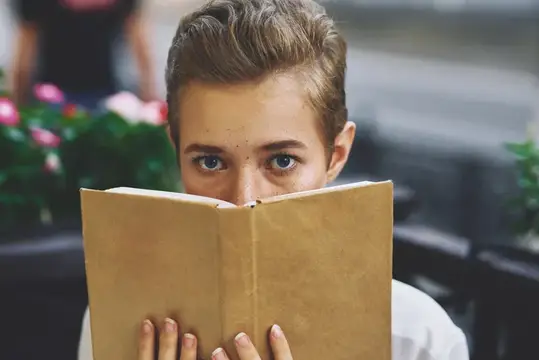 Студент с книгой в руках отдыхает и весело гуляет по городу на свежем воздухе