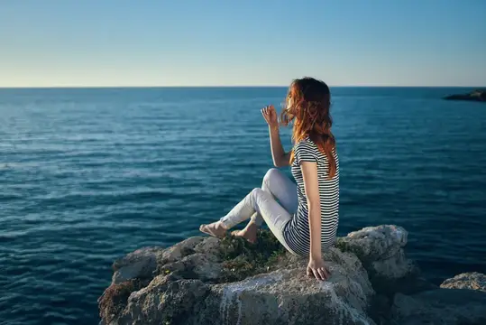 Красивая женщина на отдыхе в горах у моря, жестикулирующая руками на закате