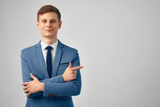 Молодой мужчина в синем костюме показывает пальцем в сторону на сером фоне