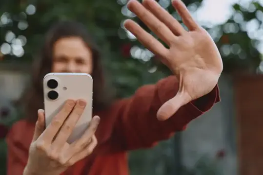 Женщина закрывает лицо рукой и фотографирует на смартфон