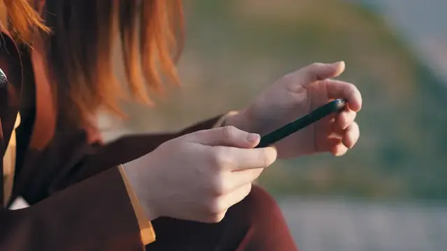 Рыжеволосая девушка держит смартфон в руках на закате