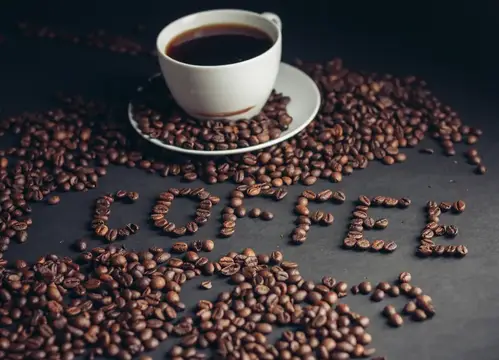 Белая чашка кофе на тёмном столе среди зёрен и надписи COFFEE