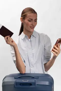 Девушка с паспортом и телефоном стоит с чемоданом