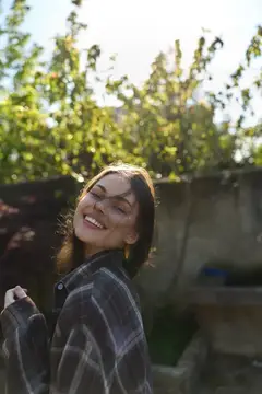 Улыбающаяся девушка в клетчатой рубашке на фоне зелени