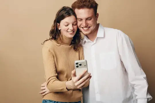 Счастливая молодая пара обнимается и делает селфи на смартфон на бежевом фоне