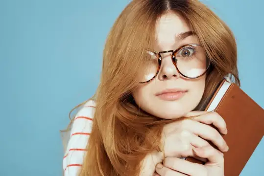 Энергичная студентка с блокнотами и в очках позирует на синем фоне