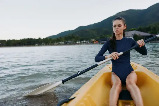 Девушка гребёт веслом в жёлтой байдарке по спокойной воде