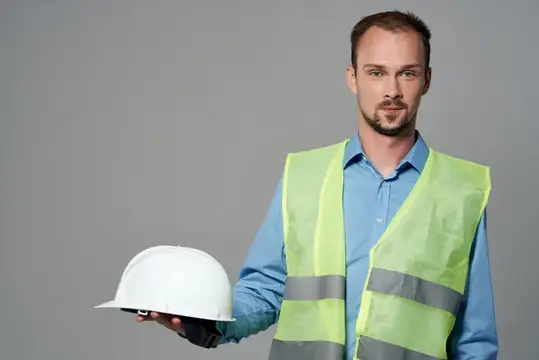 Молодой мужчина в светоотражающем жилете держит белую каску