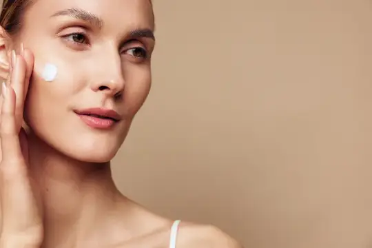 Крупный план женщины с чистой кожей, наносящей крем на щеку