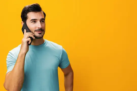 Улыбающийся бородатый мужчина говорит по телефону на жёлтом фоне