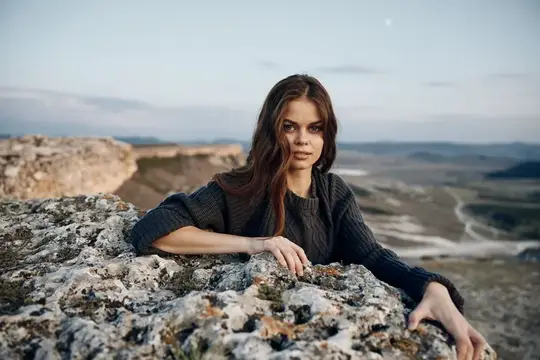 Молодая темноволосая женщина опирается на камни на фоне долины