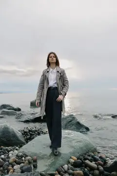 Молодая женщина в плаще стоит на камне у моря