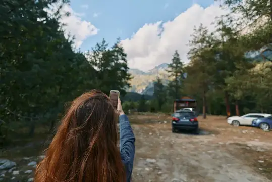 Рыжеволосая девушка фотографирует горы на телефон