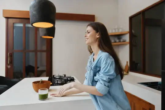 Молодая женщина в джинсовой рубашке улыбается на светлой кухне