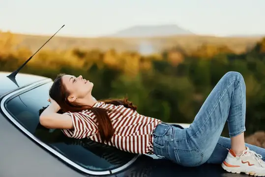 Молодая женщина лежит на капоте автомобиля на фоне гор