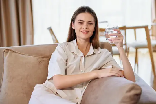 Молодая женщина в пижаме с стаканом воды на диване