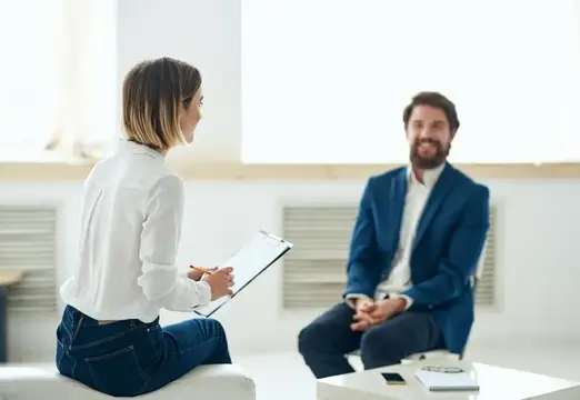 Женщина с планшетом беседует с бородатым мужчиной в светлом офисе