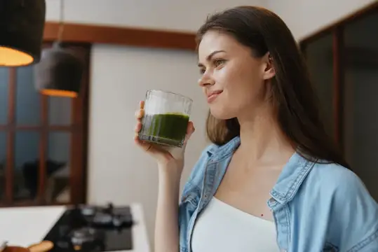 Молодая женщина с наслаждением пьёт зелёный смузи на кухне