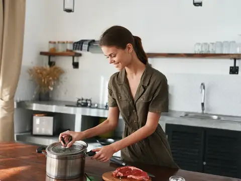 Молодая женщина готовит мясо в кастрюле на светлой кухне