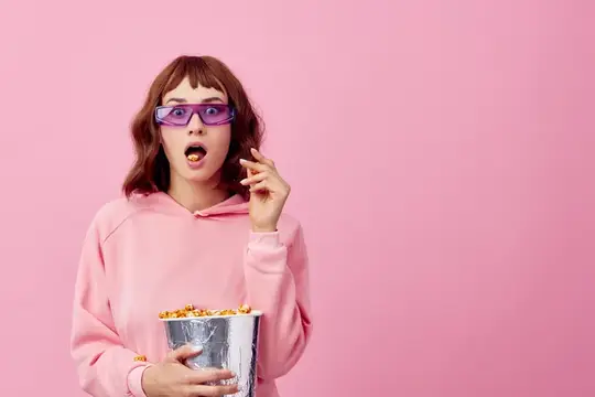 Удивлённая девушка в 3D-очках с попкорном на розовом фоне