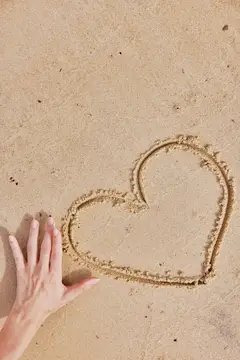 На песке пляжа рядом с уже существующим сердечком нарисовано ещё одно сердце от руки