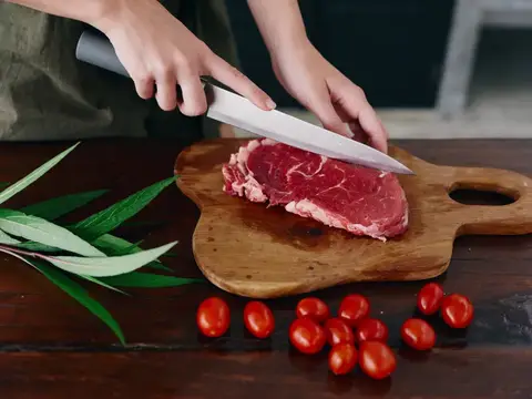 Руки нарезают сырой стейк ножом на деревянной доске