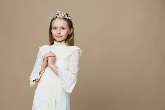 Светловолосая девочка в белом платье и короне на бежевом фоне