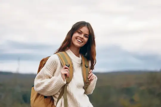 Улыбающаяся девушка с рюкзаком на фоне холмов