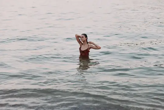 Молодая женщина в бордовом купальнике стоит по грудь в воде