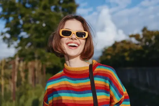 Улыбающаяся девушка с каре в желтых очках и полосатом свитере на улице
