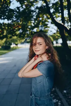 Молодая девушка с длинными волнистыми волосами в джинсовом платье на аллее парка