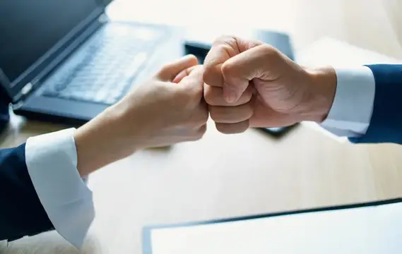 Сотрудники пожимают друг другу руки на работе в офисе, рядом документ о соглашении и ноутбук