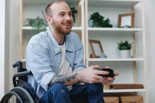 Улыбающийся парень в инвалидной коляске играет в видеоигры дома
