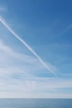 Белый след самолёта в ясном небе над морем