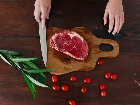 Женщина с ножом в руке нарезает свежий стейк из мяса для запекания на кухне