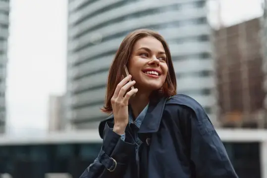 Улыбающаяся молодая женщина говорит по телефону на фоне высоток