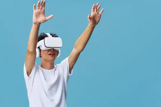 Молодой человек в VR-очках с поднятыми руками на голубом фоне