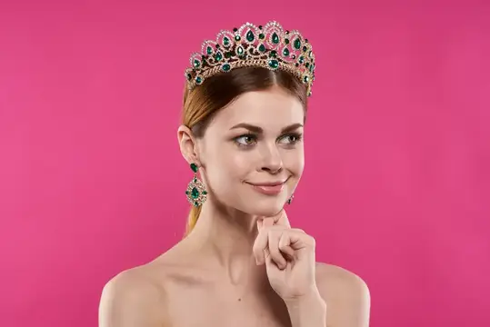 Молодая женщина в изумрудной тиаре на розовом фоне