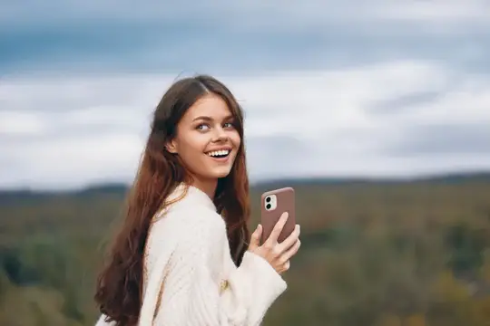 Улыбающаяся девушка с телефоном на фоне осеннего пейзажа