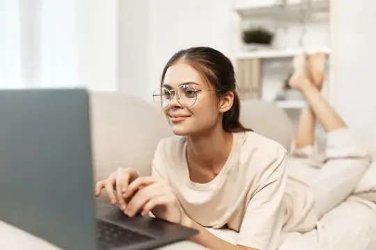 Улыбающаяся женщина работает за ноутбуком в уютной гостиной, наслаждаясь своей работой фрилансера