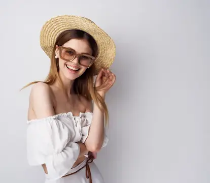 Улыбающаяся девушка в соломенной шляпе и очках на сером фоне