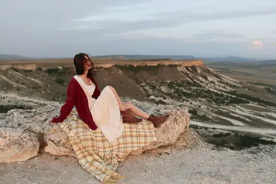 Женщина сидит на вершине скалы, наслаждаясь горным видом в дикой природе