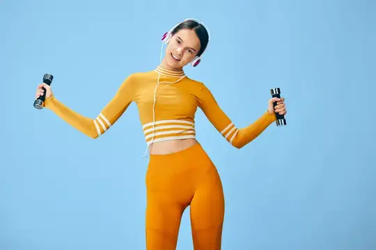 Улыбающаяся девушка в оранжевом спортивном костюме с гантелями и наушниками