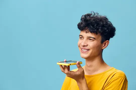 Молодой человек улыбается, пользуясь смартфоном, и демонстрирует функцию голосового помощника на фоне ярко-голубого фона