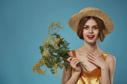 Улыбающаяся девушка в соломенной шляпе с букетом мимозы на голубом фоне