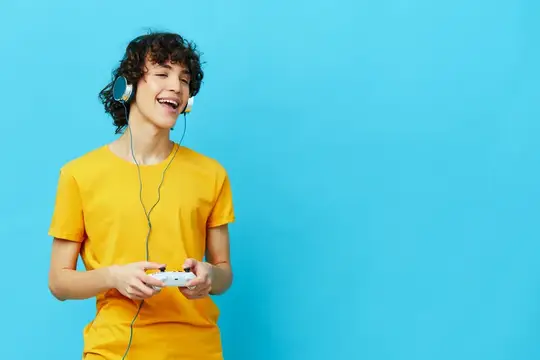 Кудрявый парень играет с джойстиком в желтой футболке на синем фоне