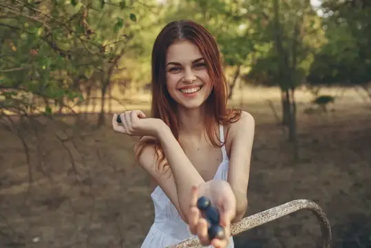 Улыбающаяся рыжеволосая девушка в белом платье в летнем саду