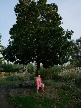 Ребёнок сидит под высоким деревом в парке, наслаждаясь природой