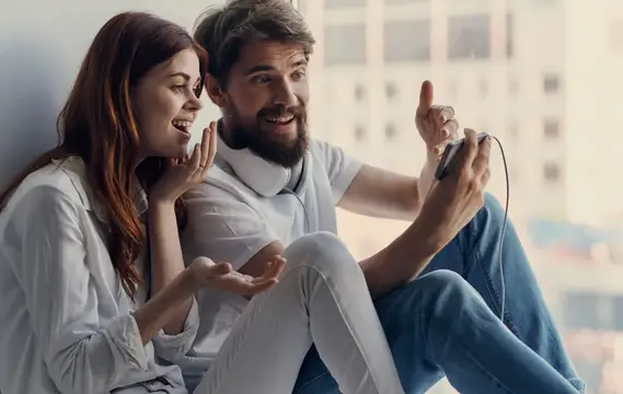 Улыбающиеся парень с девушкой играют в видеоигру у окна