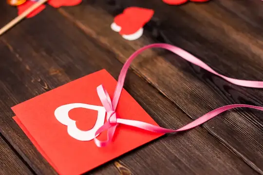 Красная открытка с белым сердцем и розовой лентой на деревянном столе